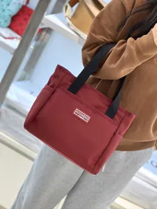 Close-up detail view of red canvas tote bag featuring black handles and handy front pocket.