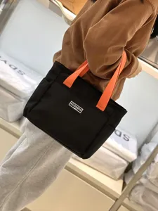 Close-up view of the black canvas tote bag featuring vibrant orange handles for daily commute.