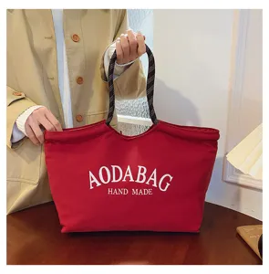 Gedetailleerd overzicht van de rode canvas tote tas met stijlvolle letteropdruk en handige handvatten.