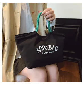 Zwarte canvas tote bag met groene touw handvatten en witte letteropdruk voor dagelijks gebruik.