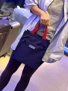 Detail shot of the dark blue bento bag with contrasting red handles and front zippered pocket.