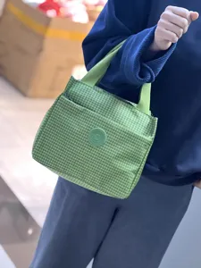 Detail van groene geruite lunchtas met stofstructuur en handig voorvak voor pendelaars.