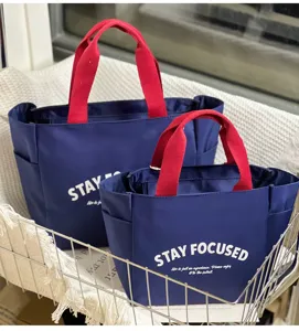 Detailansicht der marineblauen Oxford-Stoff-Lunchtasche mit roten Griffen und weißem Text.
