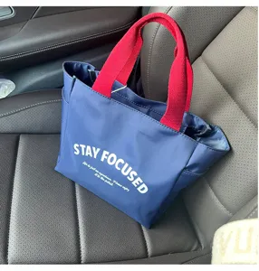 Detailaufnahme der blauen Oxford-Stoff-Tasche mit roten Henkeln und Aufdruck.