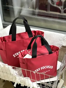 Detailansicht der roten Oxford Stoff Lunchtasche mit schwarzen Henkeln und Front Aufdruck.