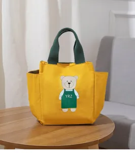 Gedetailleerd shot van de gele canvas lunchtas met een schattige berenprint en groene handvatten.