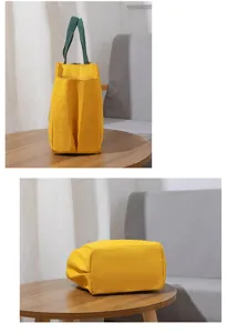 Gedetailleerd overzicht van gele canvas lunchtas met groene handvatten op houten tafel.