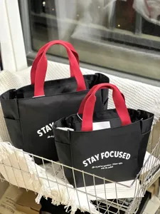 Detail shot of color-blocked oxford cloth lunch tote bag with red handles and text print.