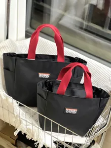 Detail view of the black and red color-blocked oxford cloth tote bag showing red handles.
