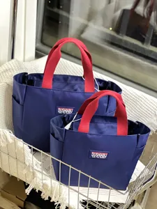 Detailansicht blaue Oxford-Stoff-Lunchtaschen mit roten Griffen und Logo-Patch vorne.
