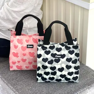 Canvas lunch bag detail showcasing cute heart pattern, durable black handles and compact shape.