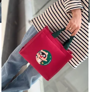 Dettaglio della borsa porta pranzo in tela rossa con manici verdi e stampa di procione.