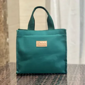 Vista dettagliata di una borsa porta pranzo in tela verde scuro con etichetta in pelle.