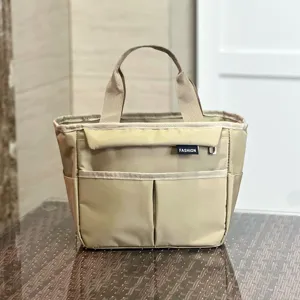 Detail view of the khaki multi-pocket lunch bag, showing the front pockets and sturdy handles.