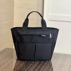 Black multi-pocket tote bag detail showing front compartments, sturdy handles, and clean stitching.