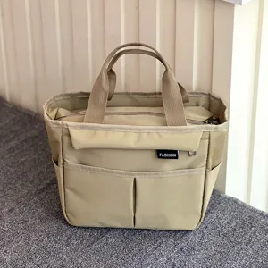 Detail view of the khaki multi-pocket canvas lunch bag showing front pocket and sturdy handles.