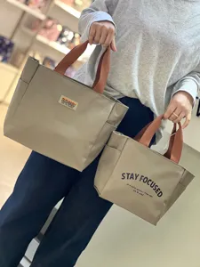 Detailansicht der Canvas-Lunchtasche mit kontrastierenden Henkeln und Front-Logodruck.