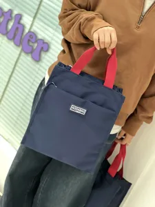 Detailed view of large color-block lunch handbag with contrast red handles and daily pocket.