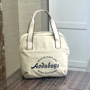 Vue détaillée du sac à main en toile beige montrant la poche avant et les poignées.