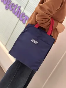 Large color-block canvas lunch bag with red handles and front pocket detail for daily use.