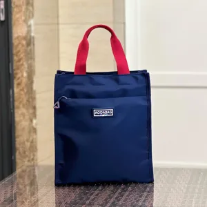 Blue lunch bag with red handles, front pocket and zipper design for daily office school use.