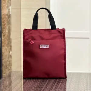 Detailed view of the large burgundy lunch handbag with black handles and front zipper pocket.