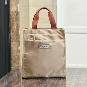 Detail view of large color-block lunch tote bag with brown handles and front zip pocket.