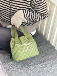Gros plan sur le sac à lunch à carreaux verts avec cordon et poignées pratiques.