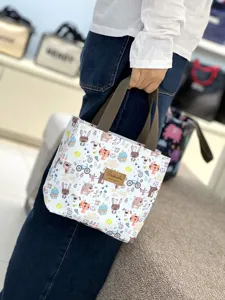 Detail shot of a small portable cartoon lunch bag with cute animal patterns and sturdy handles.