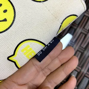 Close-up detail of canvas cup sleeve, featuring yellow smiley face print and black fabric label.