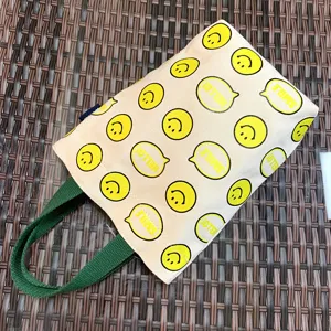 Canvas tote bag for thermos cup with cute yellow smiley face pattern and green handles.