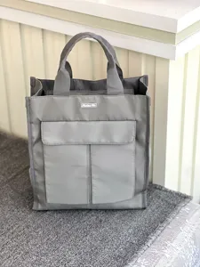 Grey multi-pocket tote bag detail, front pocket storage design, sturdy fabric handles.