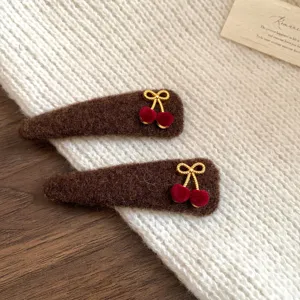 Close-up details of brown plush hair clips with gold bows and cute red cherry charms.