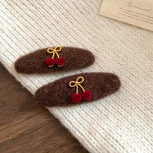 Detailed shot of brown plush hair clips with gold bows and red velvet cherry charms for women.