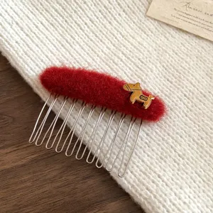 Red plush hair comb detail view, featuring gold metal animal charm and silver teeth.