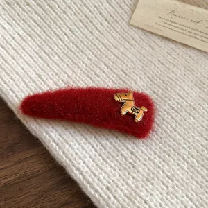 Detailed close-up of a red plush hair clip featuring a cute gold pony charm on knit texture.