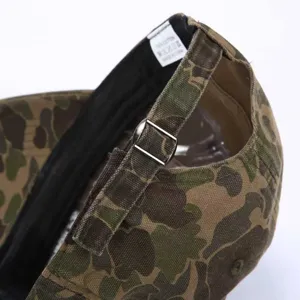 Close-up detail of camo baseball cap back strap with metal buckle and cotton label.