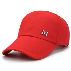Detalle de gorra de béisbol roja de lona con logotipo M de metal plateado y visera.