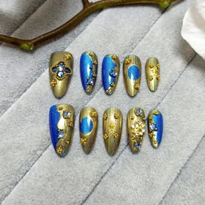 Set de uñas postizas hechas a mano con diseño lujoso azul y dorado y pedrería brillante.