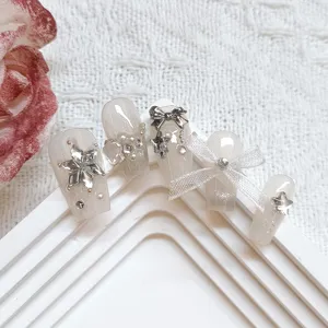 Primer plano de uñas postizas hechas a mano con efecto ojo de gato, estrellas y lazos.