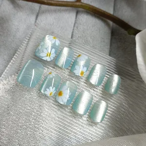 Close-up detail of handmade press-on fake nails with blue cat-eye and white daisy design.