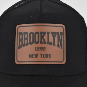 Close-up detail of the black mesh baseball cap featuring a stylish brown leather patch.