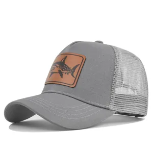 Detalle de gorra trucker gris de malla, con parche de cuero marrón y llamativo diseño de tiburón.