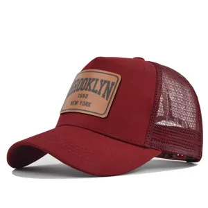 Close-up of maroon trucker hat with brown leather patch and breathable mesh back detail.