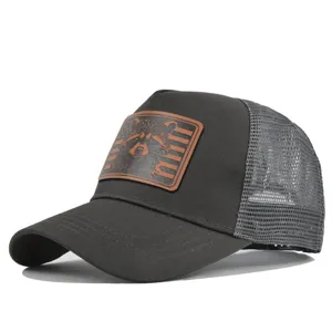 Closeup detail view of dark grey trucker baseball cap with mesh back and brown patch.