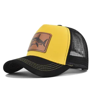 Vista detallada de gorra trucker amarilla y negra de malla con parche de tiburón de cuero.