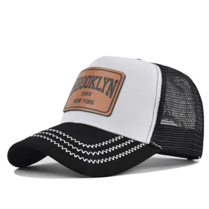 Detail shot of the black and white trucker hat featuring a stylish brown leather patch front.