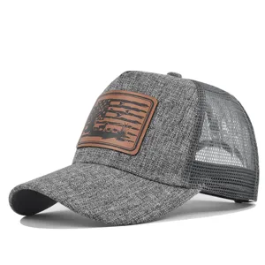 Grey trucker hat detail showing textured fabric, mesh back, and brown embossed leather patch.