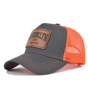 Grey trucker baseball cap with orange mesh back and brown Brooklyn leather patch detail.