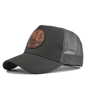Gorra trucker gris oscuro con parche de cuero marrón redondo y malla trasera transpirable de verano.